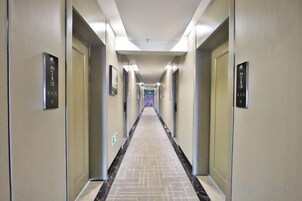 A hotel hallway with doors on both sides, a tiled floor, and a light-colored ceiling.