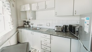 Una cocina moderna con armarios blancos, un lavamanos de acero inoxidable, un tostador y un refrigerador.