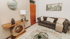 Una sala de estar con un sofá marrón, un espejo redondo, una mesa consola de madera y un cuadro en la pared.