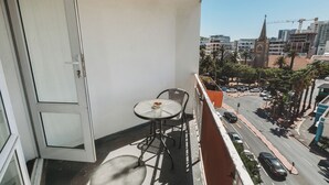 Un balcón con una mesa y sillas, con vista a una calle con coches y edificios.