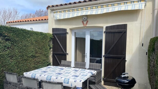Une terrasse extérieure avec des meubles en osier, un barbecue et une table couverte.