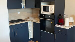 Une cuisine compacte avec des meubles de couleur sombre, un four à micro-ondes, une cafetière rouge et une table avec un set de table.