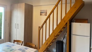 Une cuisine avec des meubles de rangement en bois, une table à manger avec des chaises, un escalier en bois et un réfrigérateur.