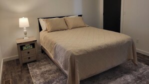 Et soveværelse med seng, natbord, lampe og en dør.