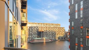 A modern building with multiple windows and balconies, a canal in the foreground, and a clear sky.