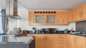 A modern kitchen with wooden cabinets, a stainless steel range hood, and a black countertop.
