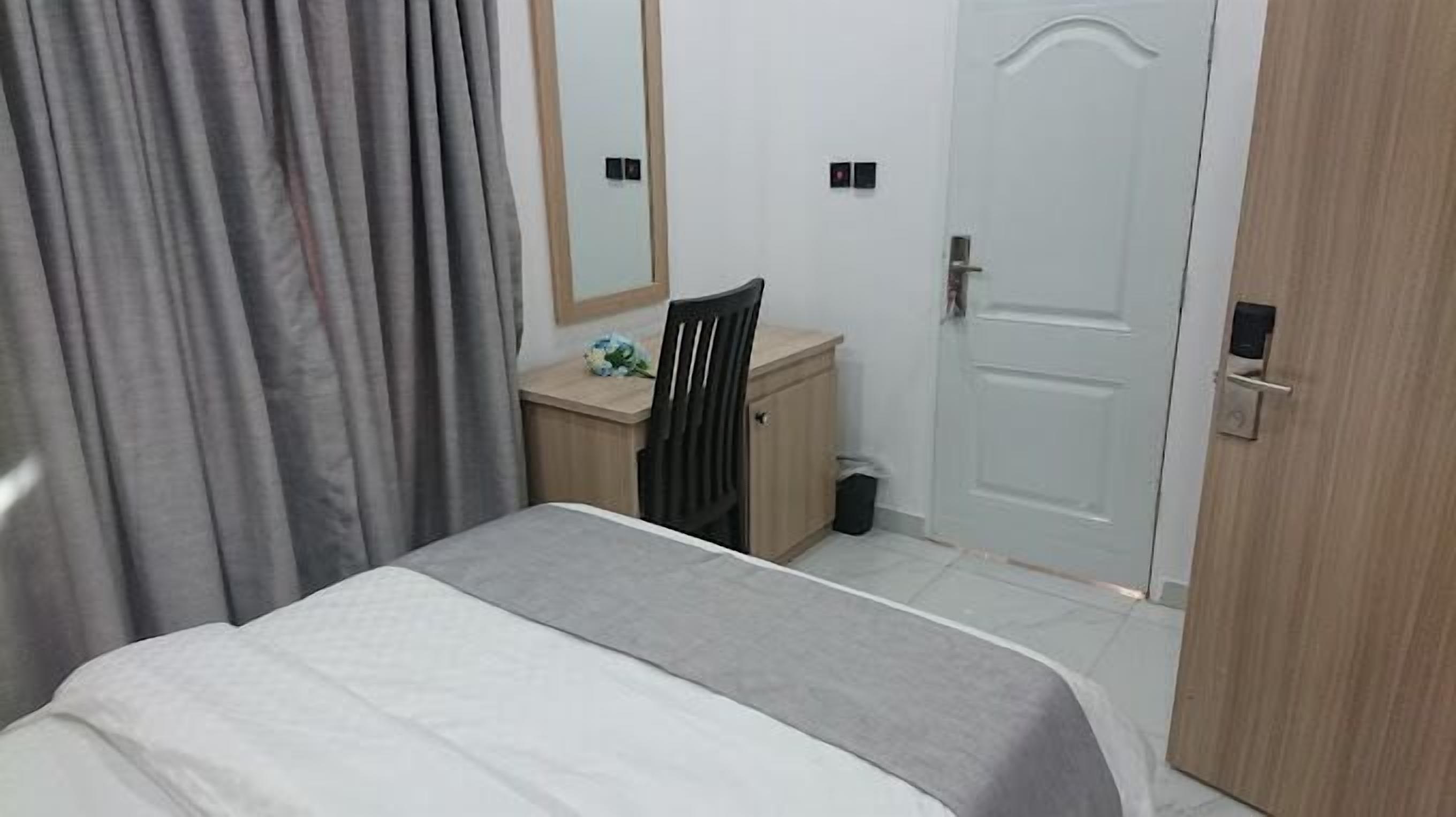 A bedroom with a bed, a desk, a chair, and a door.