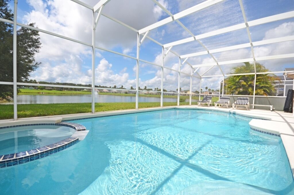 A swimming pool with a covered area, surrounded by a grassy area and a view of a lake.