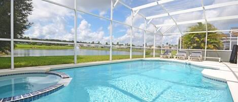 A swimming pool with a covered area, surrounded by a grassy area and a view of a lake.