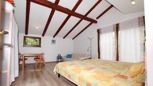 A bedroom with a wooden ceiling, a bed with a floral bedspread, a desk with a chair, and a window with curtains. - ROVINJ HOME Studio with Terrace (Rovinj)