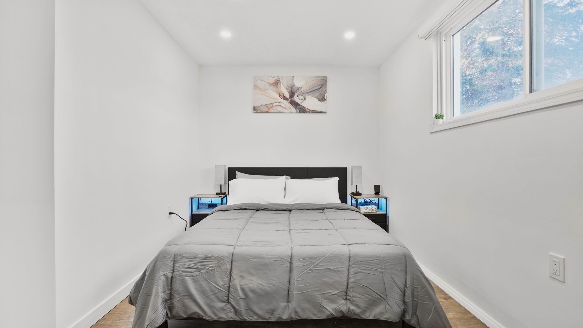 Une chambre à coucher comprenant un lit, des tables de chevet, une commode, une œuvre d’art accrochée au mur et une fenêtre donnant sur un paysage.