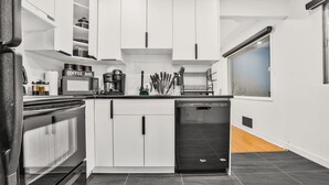 A modern kitchen with white cabinets, a coffee bar, a dishwasher, and a window with a view.