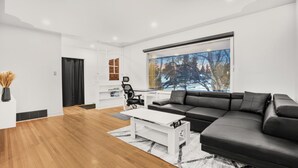 A modern living room with a black leather sofa, a white coffee table, and a large window with a snowy view.