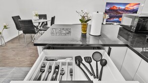 A modern kitchen with a black countertop, a drawer with utensils, a vase with flowers, and a painting on the wall.