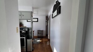 A hallway with a kitchen area visible at the end, featuring cabinets, a stove, and a refrigerator. - Charming 2-bedroom house in peaceful De Pere with WiFi. Outdoor fire pit. (De Pere)