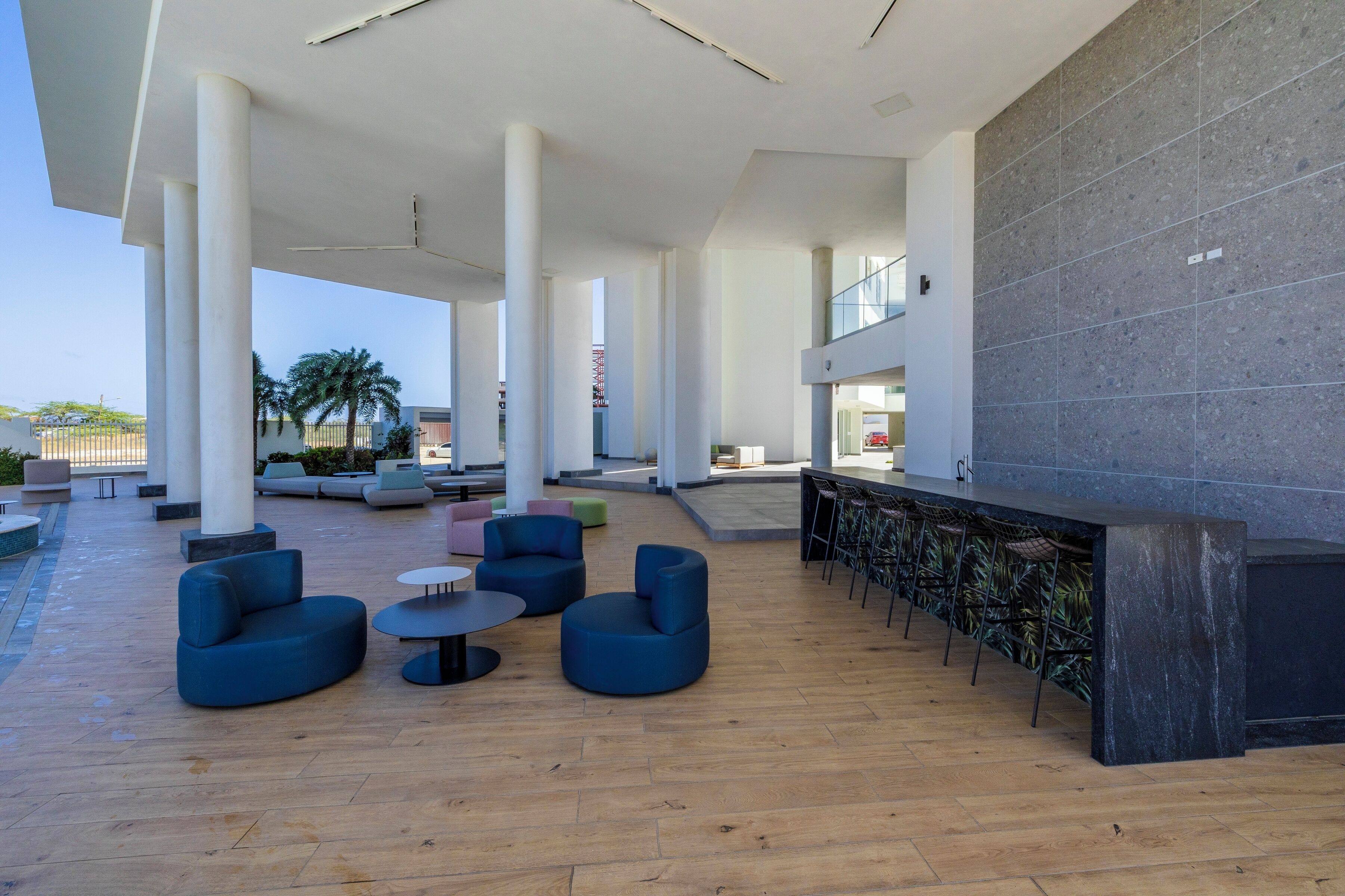 A spacious outdoor lounge area with modern seating, a bar, and a view of palm trees.