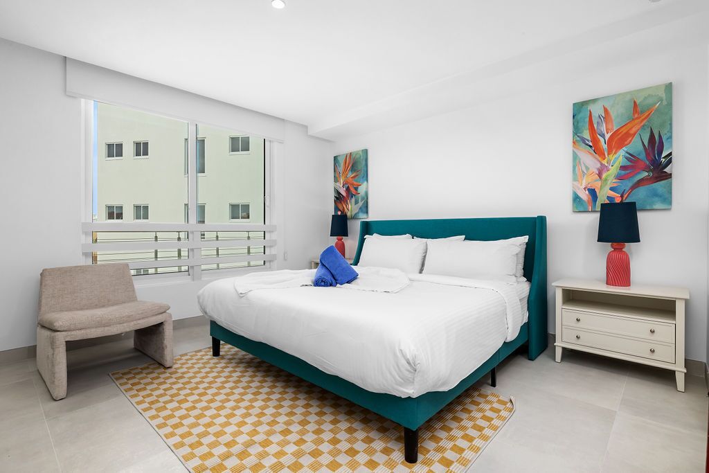 Una habitación de hotel moderna con una cama grande, un pequeño rincón de descanso y obras de arte en las paredes.