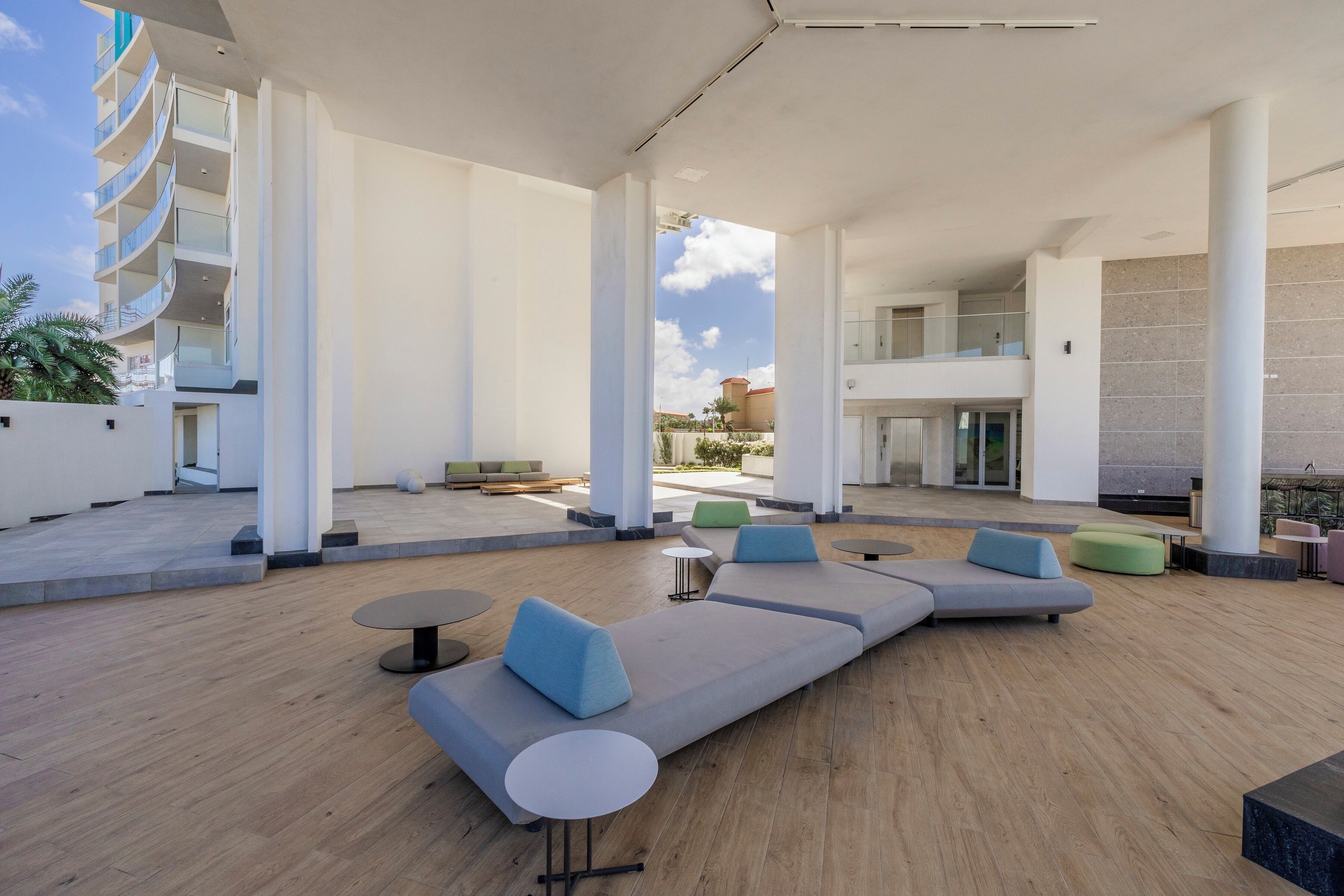 A modern outdoor lounge area with seating and tables, large pillars, and a view of a building in the background.