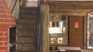 A staircase leading to a second floor, a wooden door with a 'Feminino' sign, and a small table with a mirror and a sign in Spanish. - Comfort Suite 102 - Acayaca Inn (Centro Diamantina)