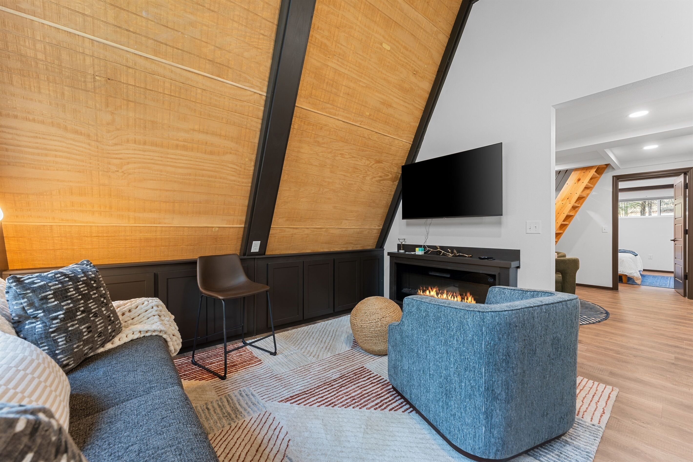 Uma sala de estar moderna com lareira, uma televisão de tela plana na parede e um espaço de estar acolhedor com uma poltrona azul e um sofá.