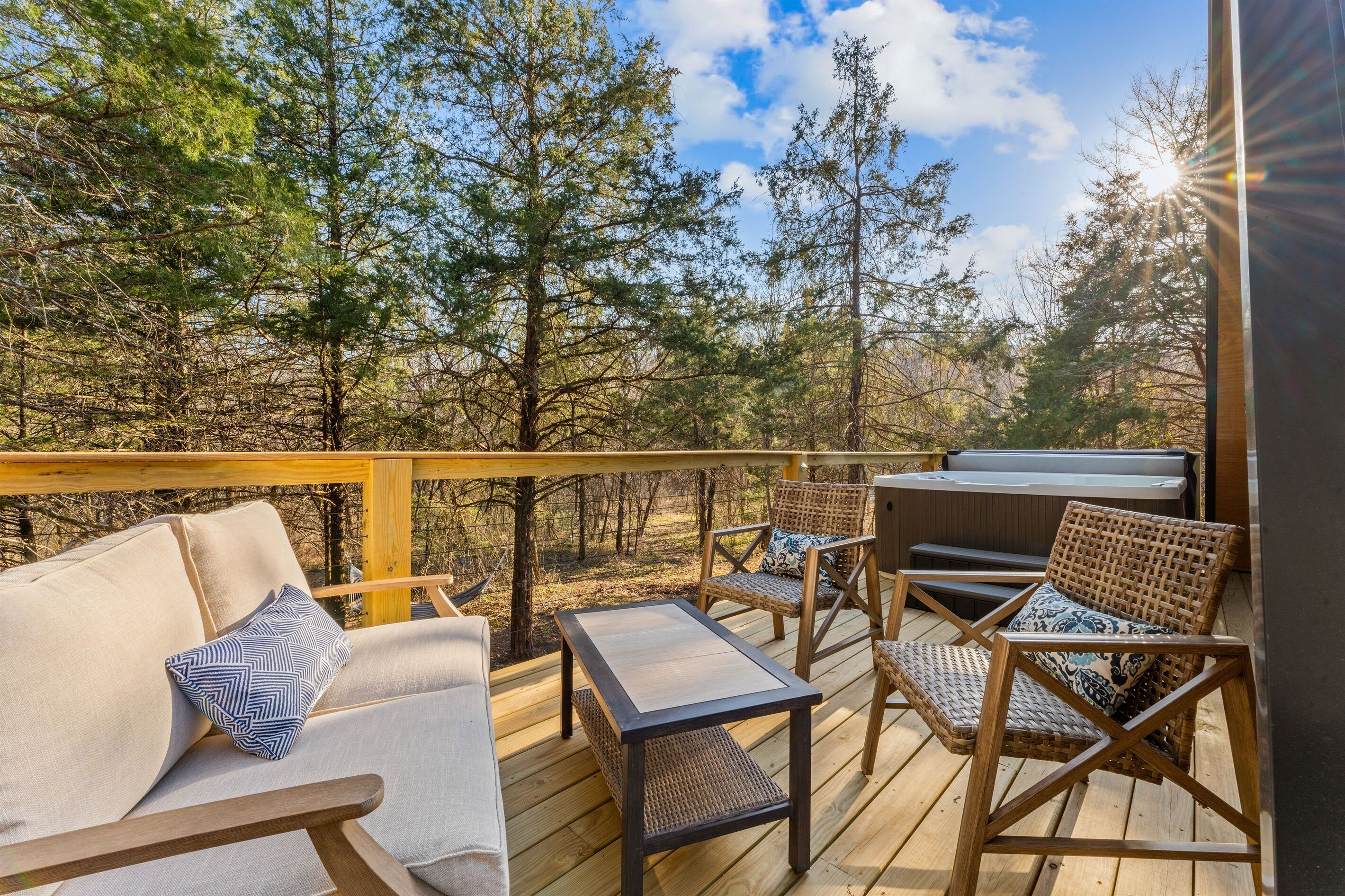A wooden deck with outdoor furniture, including a sofa and chairs, overlooking a forested area.