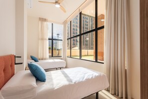 Habitación de hotel con dos camas, ventilador de techo, ventanas amplias y vista a la ciudad.