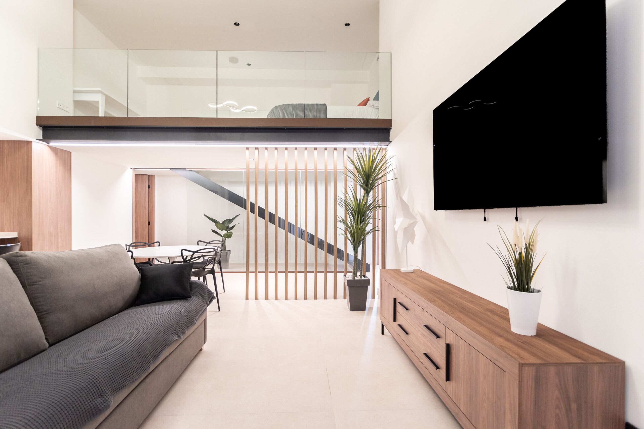 A modern living room with a sofa, a wooden cabinet, and a TV mounted on the wall.