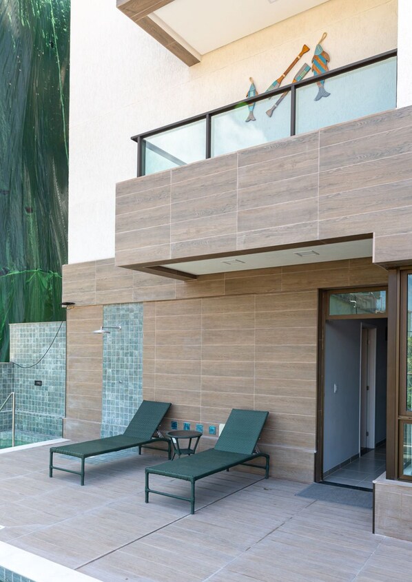 A modern building with a balcony, two lounge chairs, and a glass railing. - Moderno Agradável Flat P Galinhas BP402 (Ipojuca)