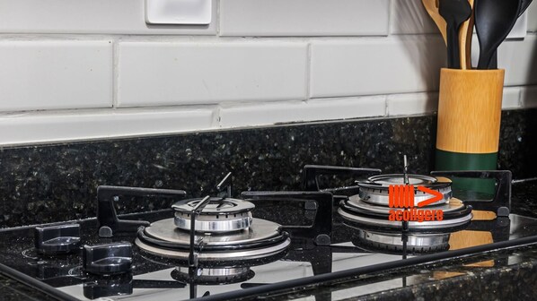 A kitchen with a gas stove, a wooden utensil holder, and a black granite countertop.