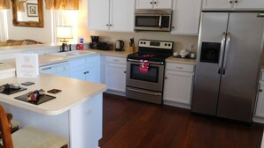 Una cocina con armarios blancos, un refrigerador de acero inoxidable, un microondas, un horno y una cafetera.