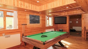 A wooden-paneled room with a pool table, a television, and a window.