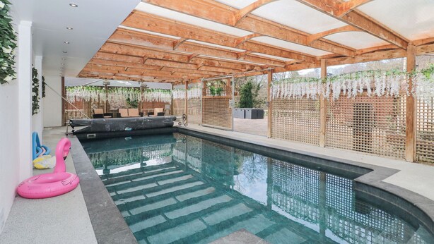 An indoor swimming pool with a wooden ceiling and a seating area with a sofa and chairs.