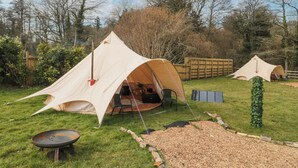 A tented camping area with a dining table and a grill.