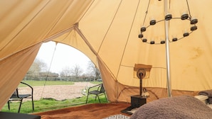 A tent with a view of a grassy field, a black chair, a patterned rug, and a heater.