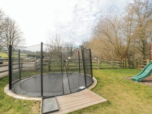 Ein Trampolin mit Sicherheitsnetz, umgeben von einem Holenzaun, in einem Rasenstück mit einer grünen Rutsche.