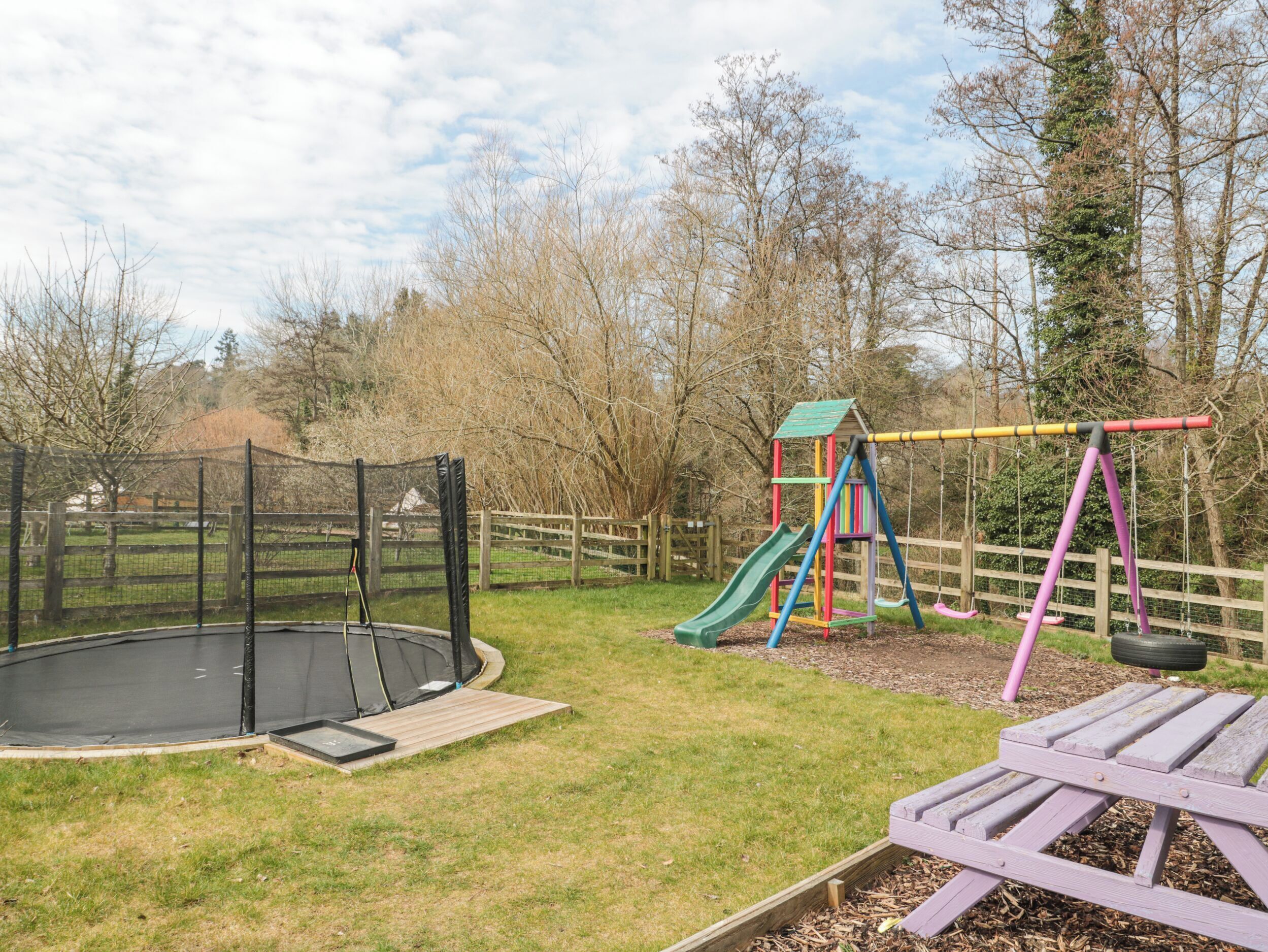 Ein Spielplatz mit Schaukeln, einer Rutsche und einem Trampolin.