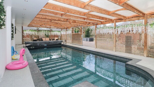 A swimming pool with a wooden pergola overhead, surrounded by a fence with hanging white flowers.