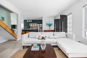 A modern living room with a white sectional sofa, a wooden coffee table, and a vase with flowers. - Metalasia Four - Three Bedroom House, Sleeps 6 (Betty's Bay)