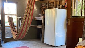 A rustic kitchen with a white refrigerator, wooden beams, a hanging hammock, and a red mat on the floor.
