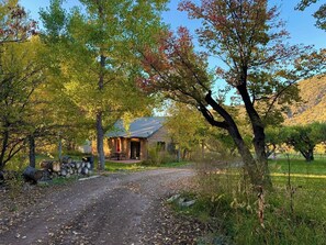 A rustic cabin with a dirt path leading to it, surrounded by trees and a grassy field.