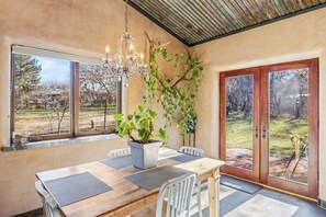 A dining area with a wooden table, chairs, a chandelier, and a potted plant. - The Vineyard House - A Serene Cottage in the Mountains with Magical Views (Dixon)