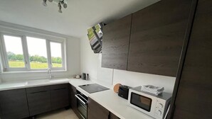 Una cocina moderna con armarios oscuros, una encimera blanca, un microondas y una ventana con vistas a zonas verdes.