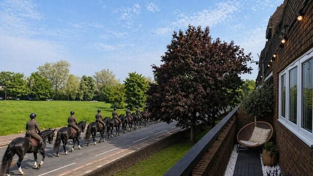 Un sendero con caballos y jinetes, un edificio de ladrillo con una ventana, y un árbol.