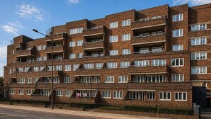 Un edificio de apartamentos de ladrillo con varios pisos, balcones, una acera pavimentada y cielo despejado.