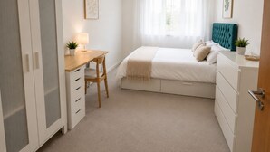 Un dormitorio con cama, escritorio, silla, armario y ventana con cortinas.