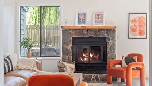 A living room with a stone fireplace, a large window, and orange chairs. - Remodeled! Beaverton 2BR/2BA Fenced Backyard Extended Stays (Beaverton)