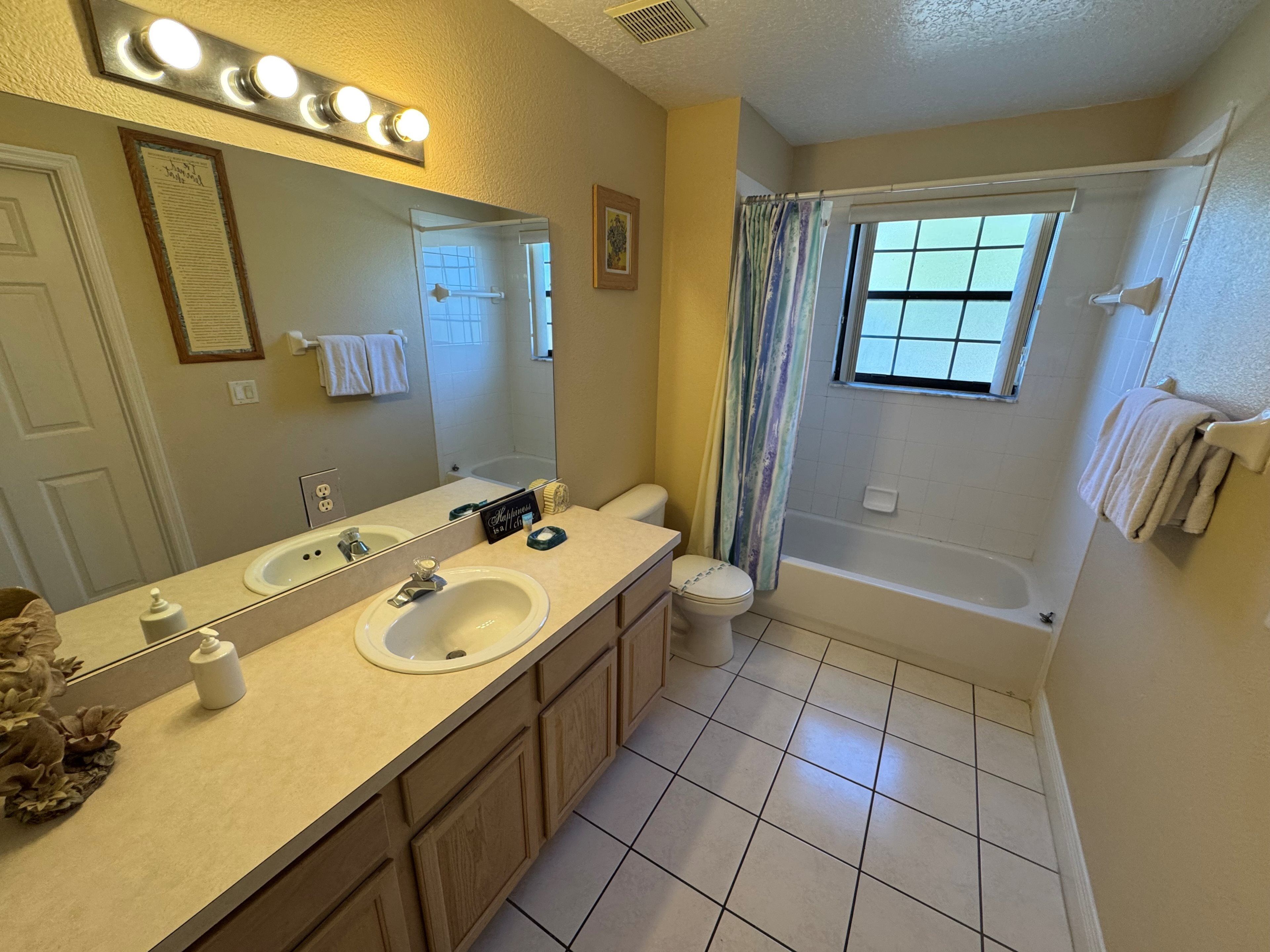 A bathroom with a double sink vanity, a toilet, a bathtub, and a window with a view.