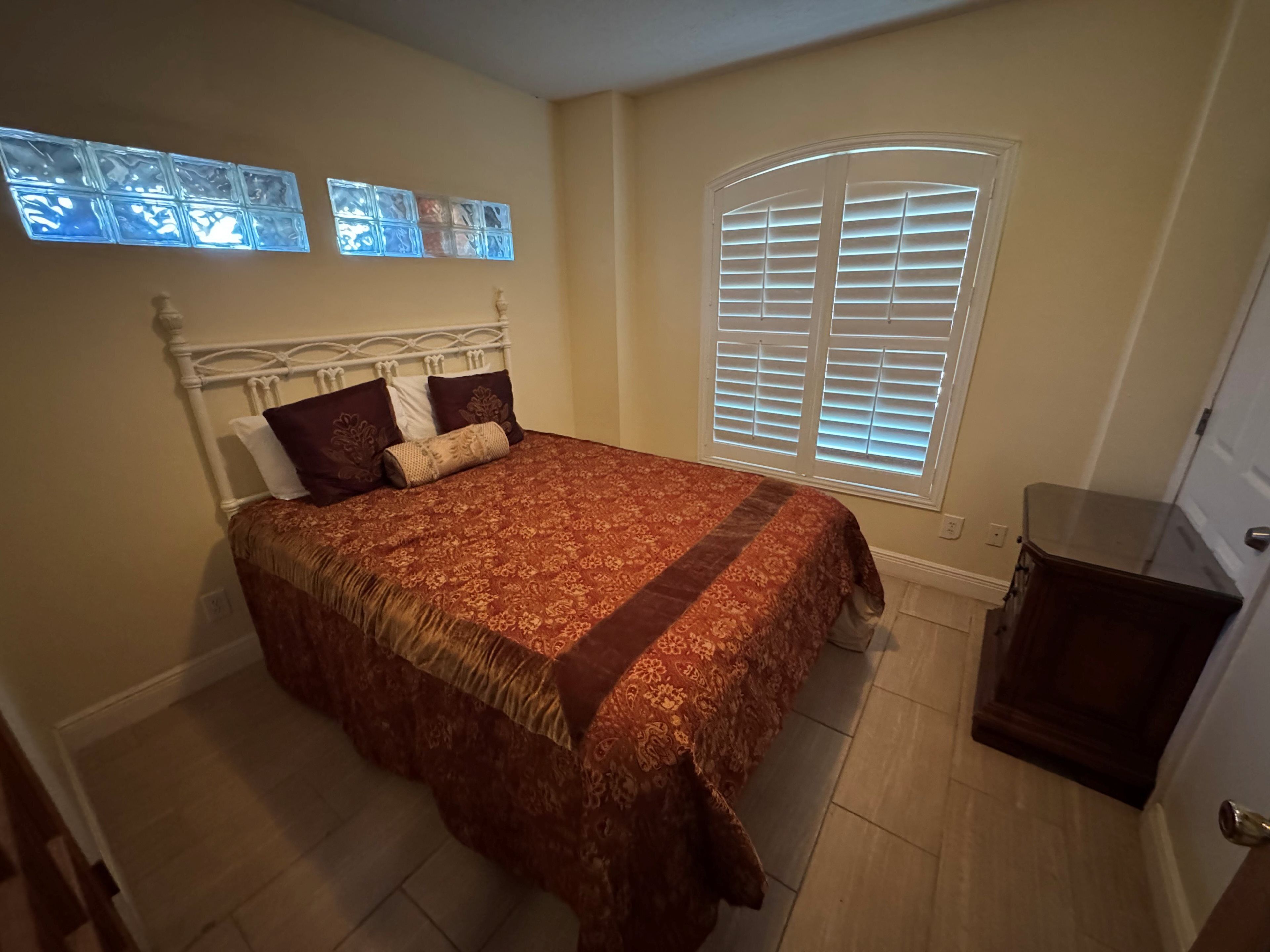 A bedroom with a bed, a window with blinds, and a door.