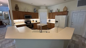 A kitchen with wooden cabinets, a microwave, a refrigerator, and a large island with a sink. - Southern Comfort on Hampton Lakes - The Ultimate Luxury Retreat! (Davenport)