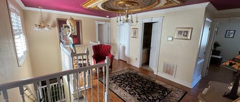 A spacious living area with a red armchair, a patterned rug, and a decorative ceiling.
